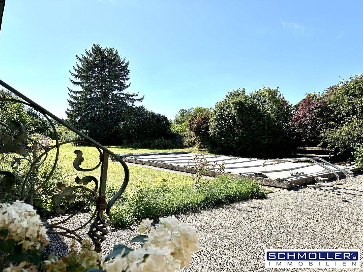 Großer grüner Garten mit einem abgedeckten Pool und hohen Bäumen unter klarem blauem Himmel.