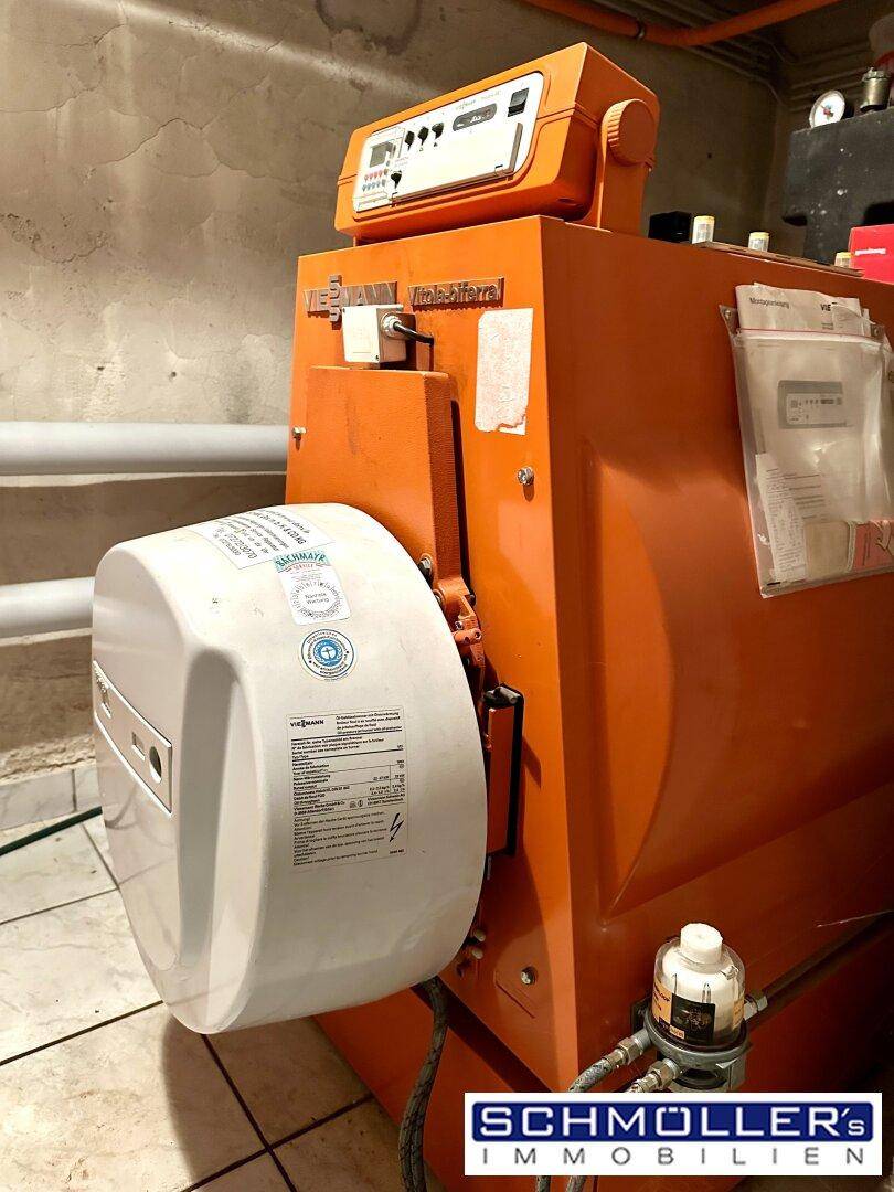 Heizraum im Keller mit einem großen orangefarbenen Heizkessel und Warmwasserspeicher.