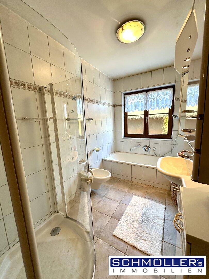 Helles Badezimmer mit Dusche, Badewanne, Bidet und Fenster, komplett gefliest.
