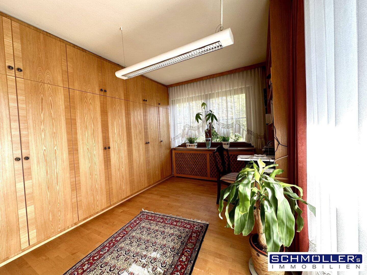Schlafzimmer mit raumhohen Holzschränken, Parkettboden und einem Fenster mit Blick ins Grüne.