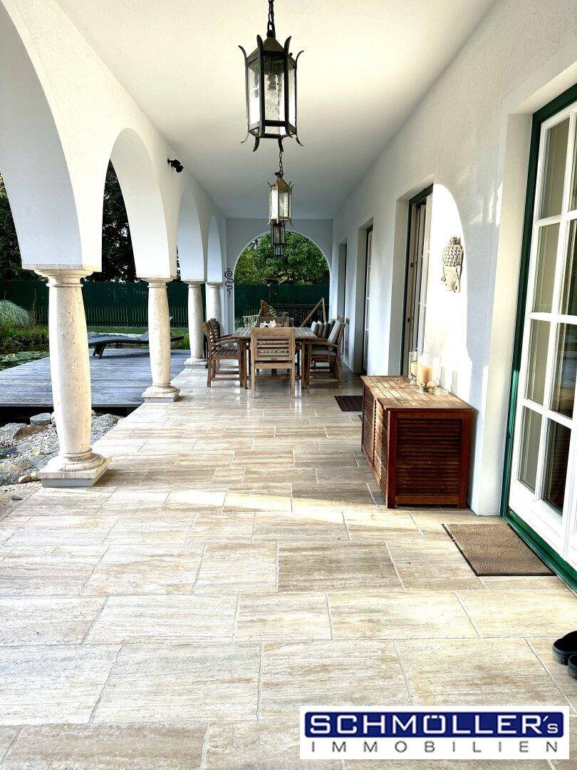 Lange, überdachte Loggia mit Fliesenboden, Säulen und traditionellen Hängelampen.