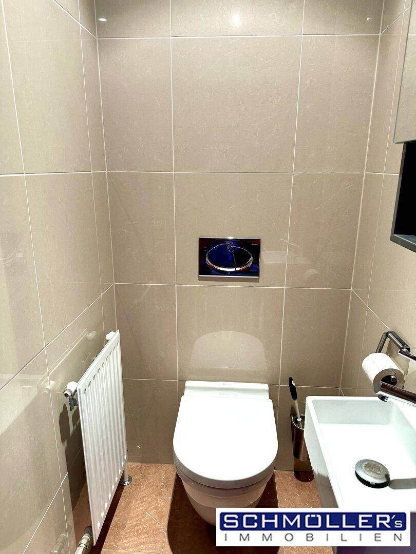 Modernes Gäste-WC mit beigefarbenen Fliesen, wandhängendem WC und kleinem Waschbecken.