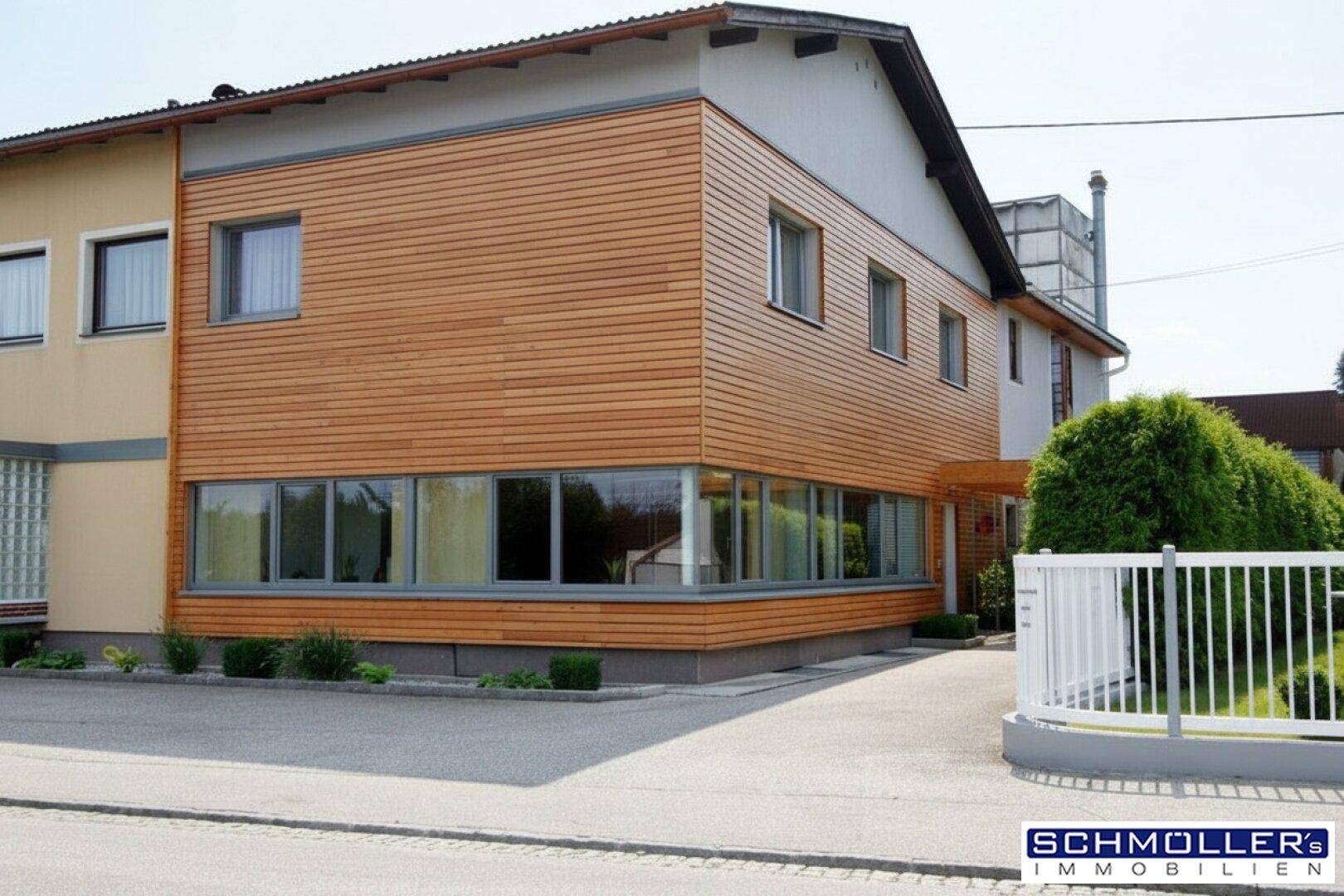 Modernes Gebäude mit Holzfassade und großen Fensterfronten, umgeben von gepflegten Grünflächen.