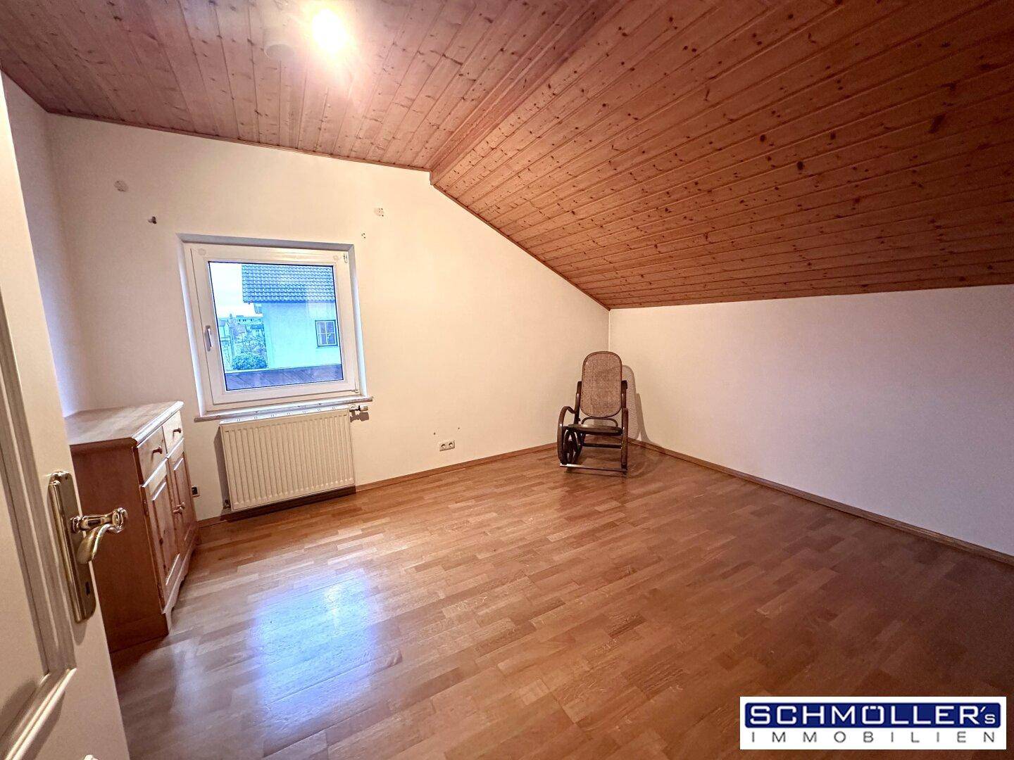 Schlafzimmer im Dachgeschoss mit Holzdecke, Parkettboden und einem Fenster mit Ausblick.
