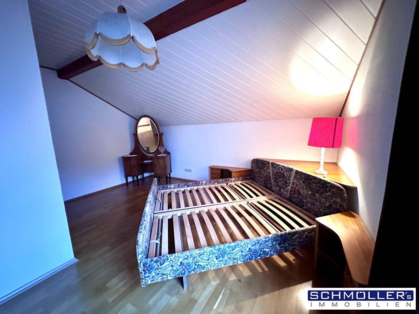 Dachgeschoss-Schlafzimmer mit Holzdecke, Parkettboden und einem Bettgestell unter schräger Decke.