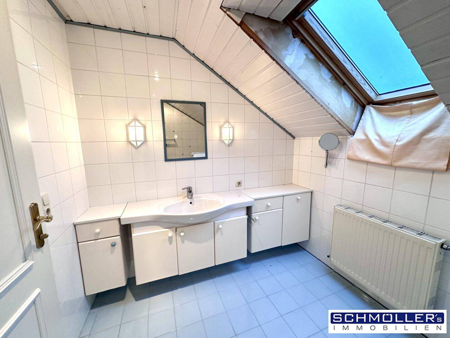 Badezimmer im Dachgeschoss mit hellblauen Fliesen, Waschtisch und Dachfenster für Tageslicht.