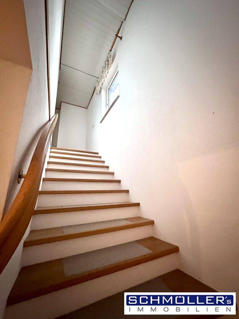 Holztreppe mit weiß gestrichenen Stufen und einem Fenster, das den Aufgang erhellt.