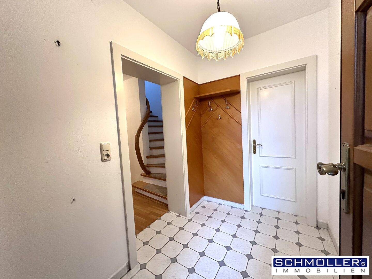 Eingangsbereich mit Fliesenboden, Garderobe und Blick auf die Holztreppe ins Obergeschoss.