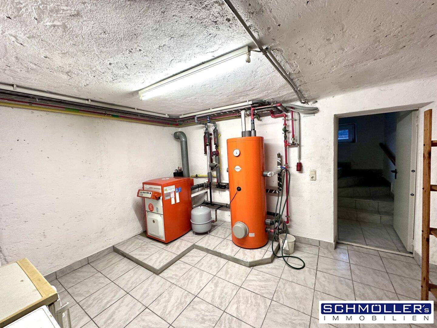 Heizungsraum im Keller mit Heizkessel, Warmwasserspeicher und Fliesenboden.