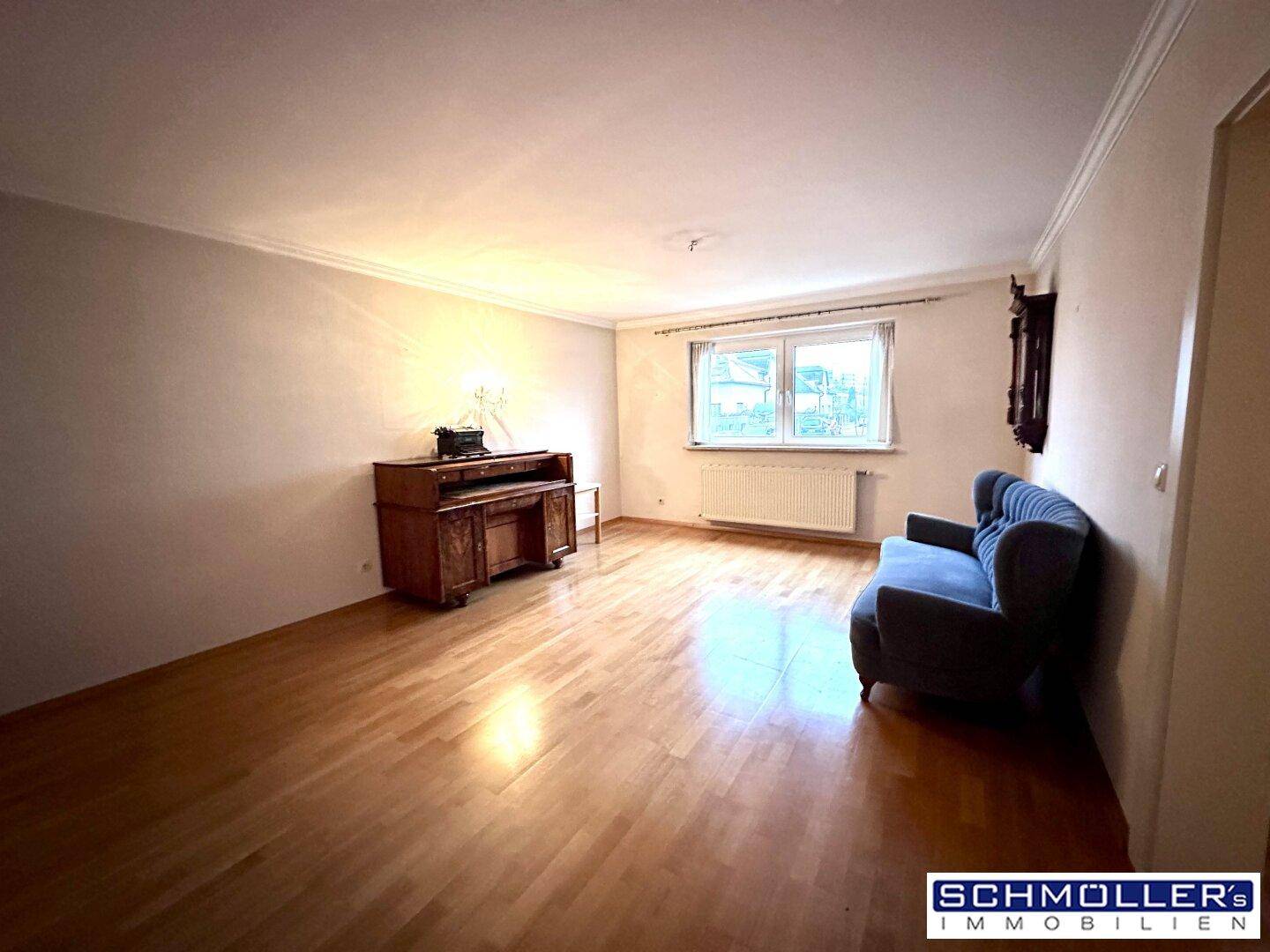 Helles Wohnzimmer mit Parkettboden, einem antiken Möbelstück und einem bequemen Sessel.