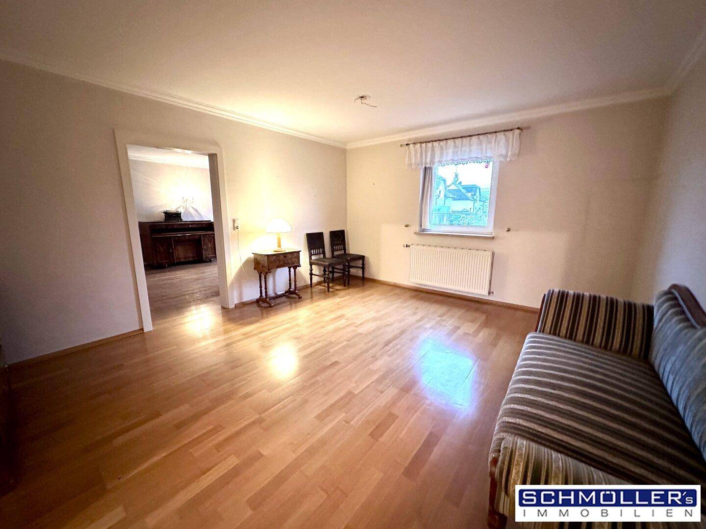 Geräumiges Wohnzimmer mit Holzparkettboden und einem Fenster, das viel Tageslicht hereinlässt.