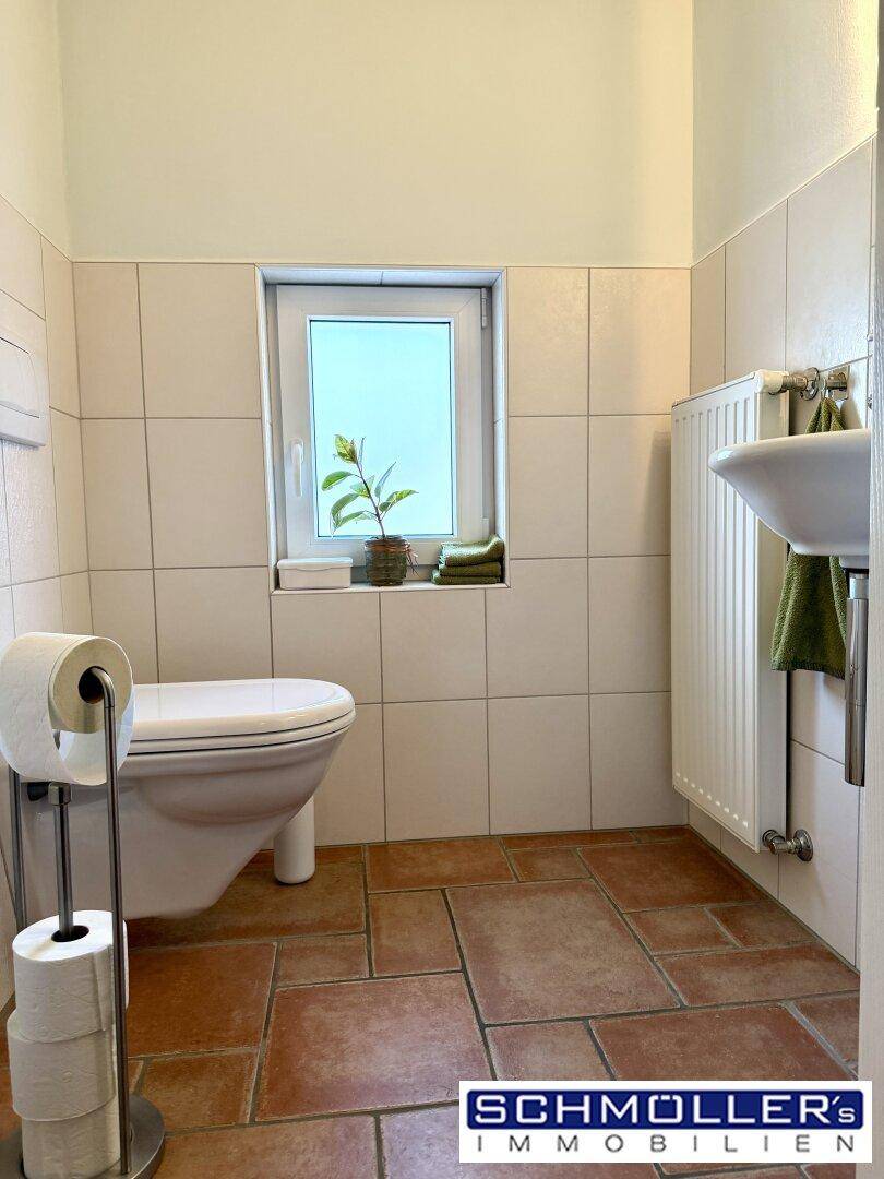 Helles Gäste-WC mit Fenster, Wand-WC und Fliesenboden in neutralen Farben.