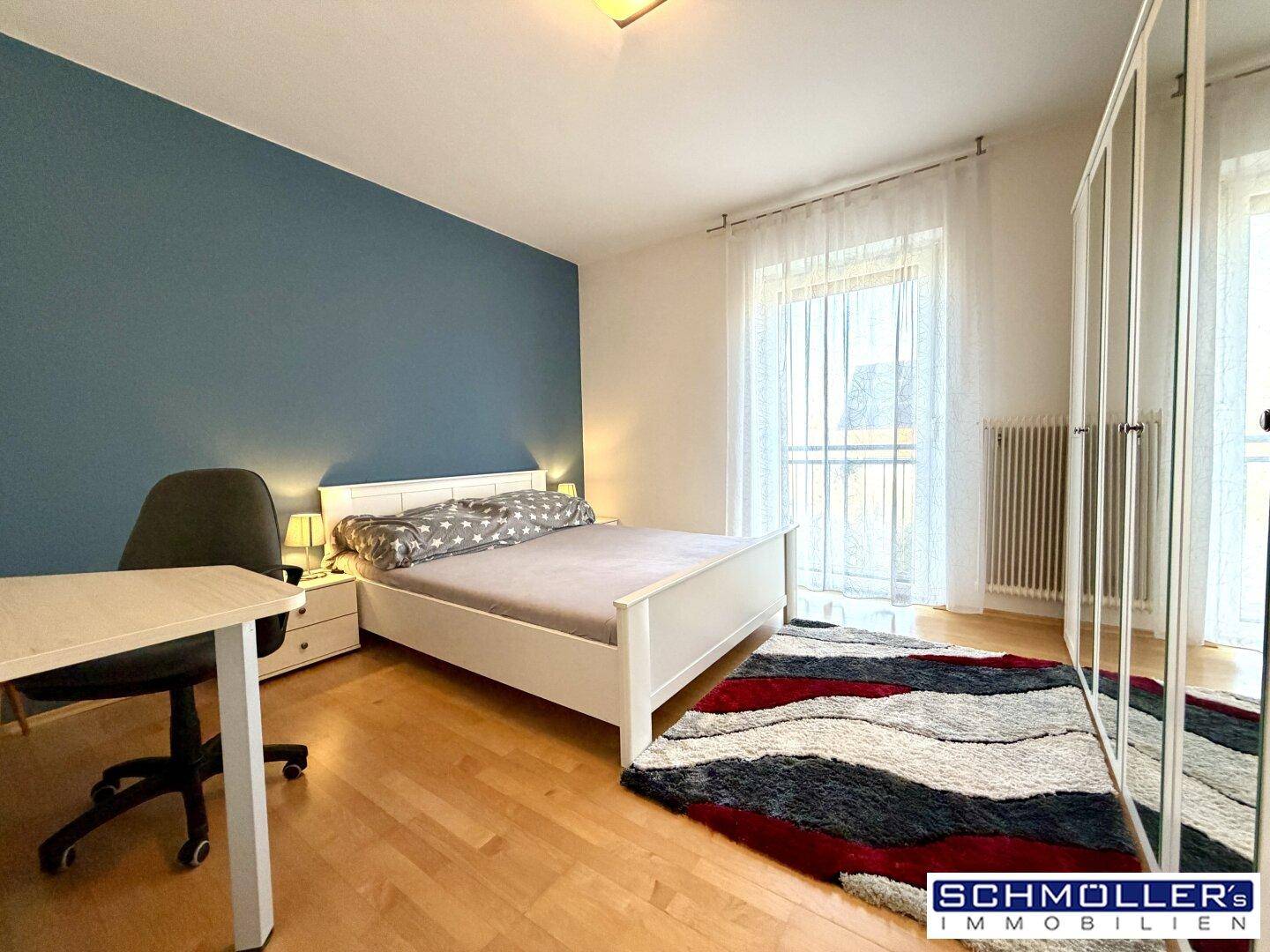 Modernes Schlafzimmer mit blauer Akzentwand, Parkettboden und Zugang zu einem französischen Balkon.
