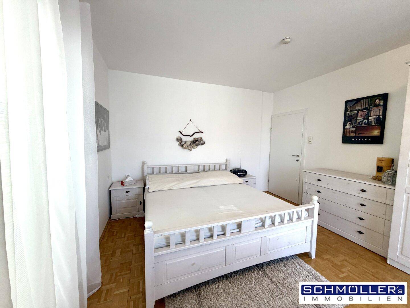 Gemütliches Schlafzimmer mit weißem Holzbett, Parkettboden und Teppich, hell und einladend.