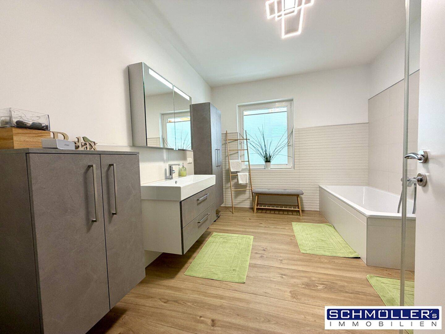 Modernes Badezimmer mit Badewanne, Einzelwaschbecken und Holzoptik-Boden, hell und funktional.