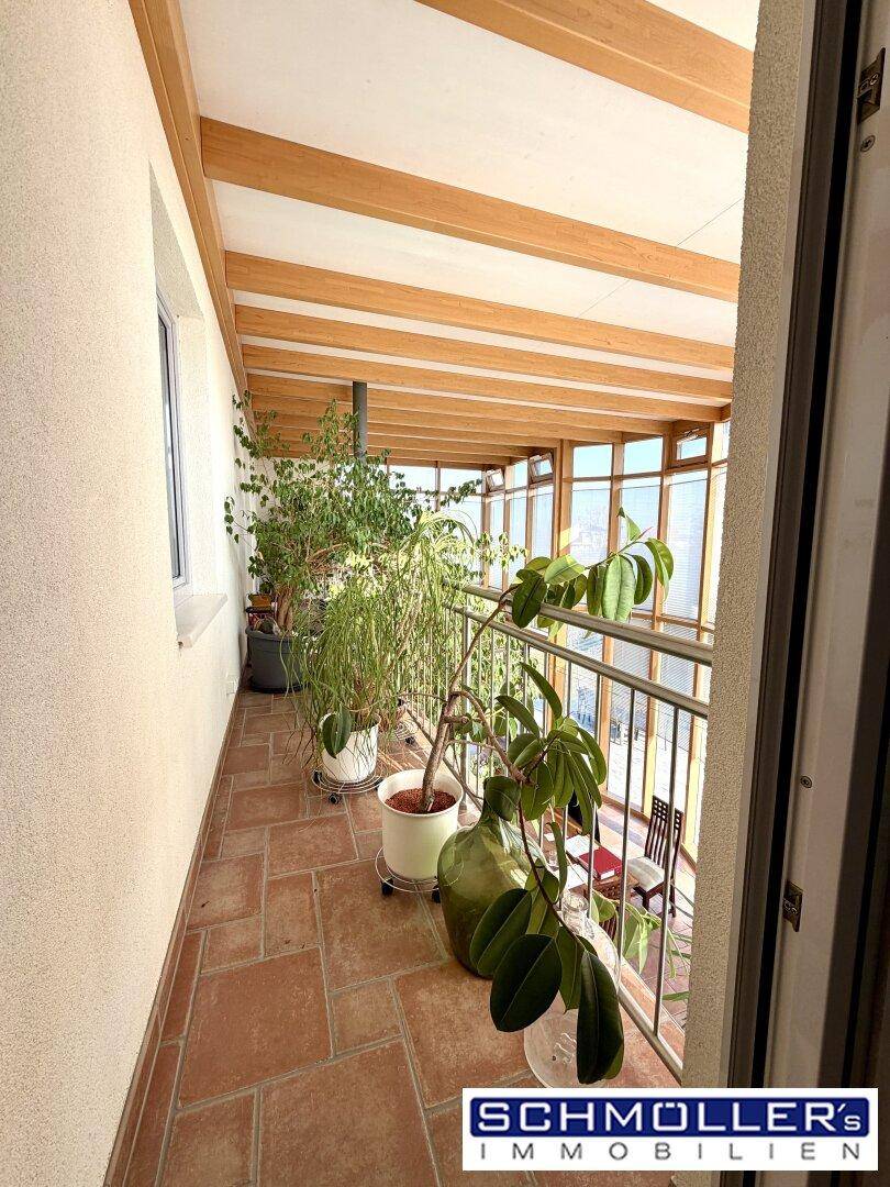 Überdachter Balkon mit Fliesenboden und vielen Pflanzen, bietet einen geschützten Außenbereich.