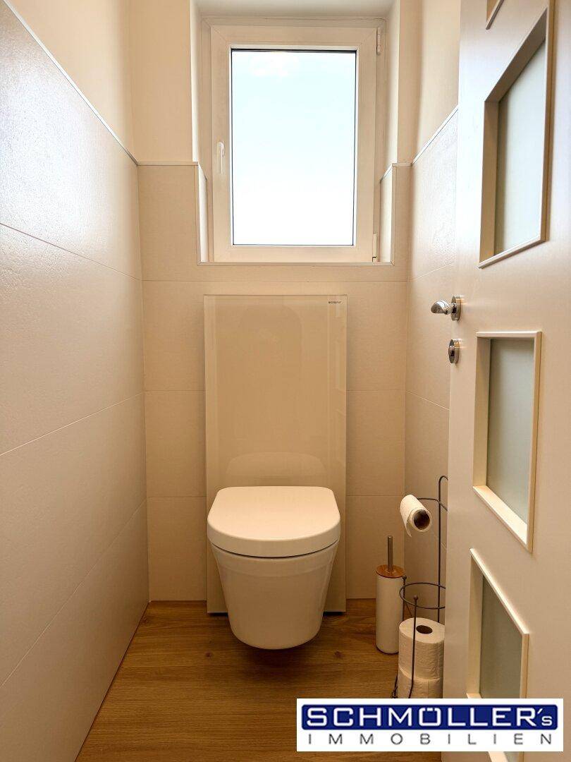 Kleines Gäste-WC mit Fenster, Wand-WC und Holzoptik-Boden, schlicht und sauber.
