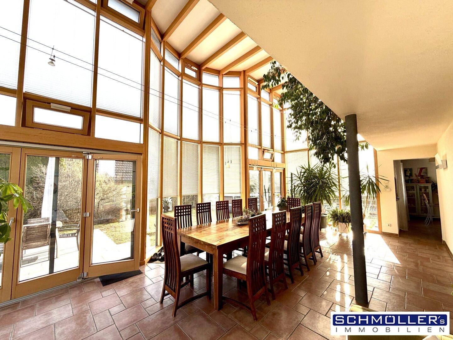 Heller Essbereich im Wintergarten mit Holztisch und Stühlen, umgeben von großen Fensterfronten.