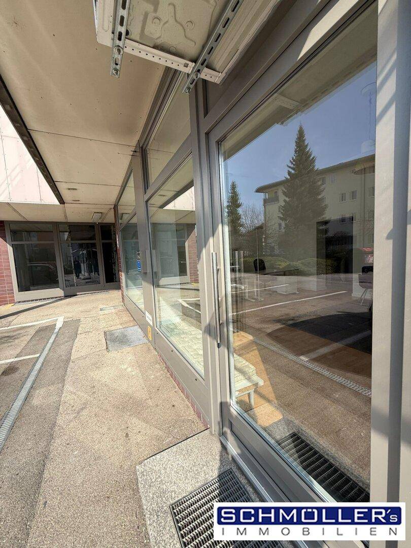 Nahaufnahme des Ladeneingangs und der Schaufensterfront, die die Umgebung im Glas widerspiegelt.