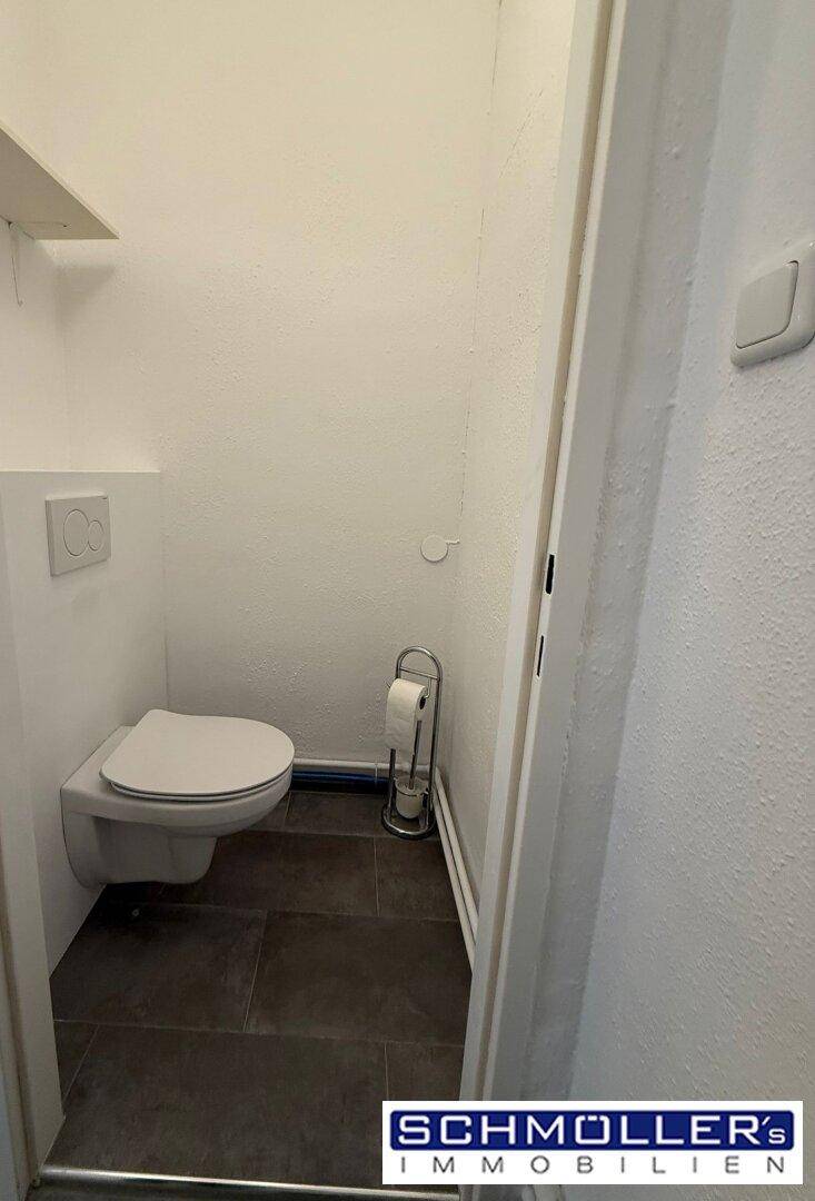 Kleiner Toilettenraum mit wandhängendem WC und dunklen Fliesen auf dem Boden.