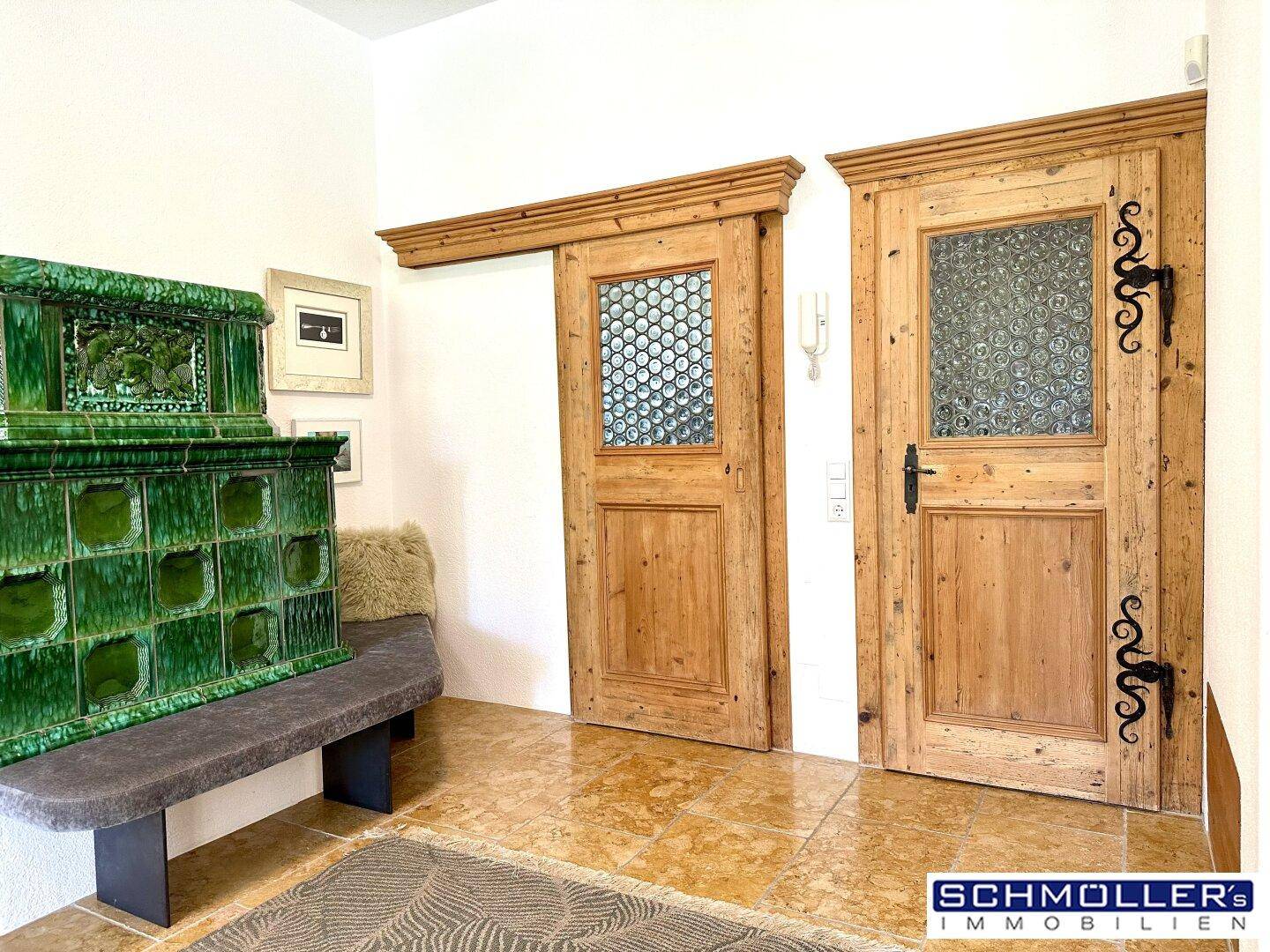 Detailansicht eines grünen Kachelofens und rustikaler Holztüren mit schmiedeeisernen Beschlägen.