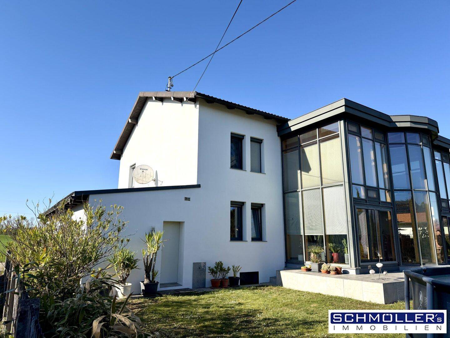 Rückansicht des Hauses mit Gartenbereich und dem modernen Glasanbau unter blauem Himmel.