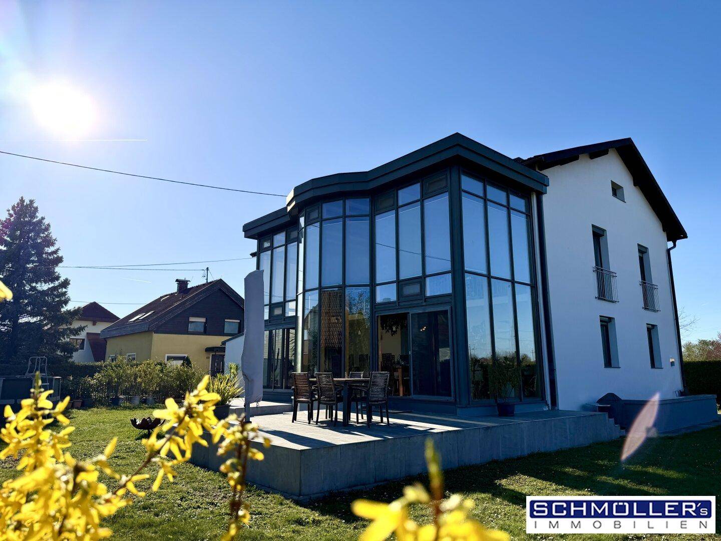 Sonnige Terrasse mit Gartenmöbeln und Blick auf den modernen Glasanbau des Hauses.