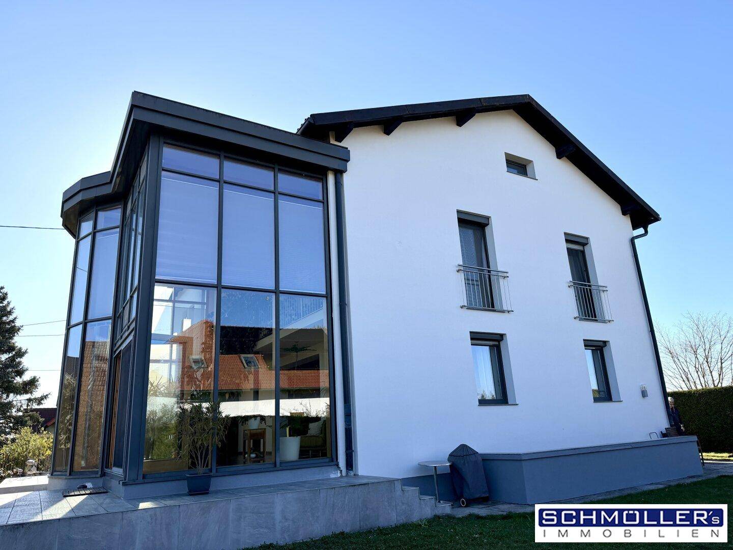 Moderne Hausfassade mit großem Glasanbau und kleinen französischen Balkonen im Obergeschoss.