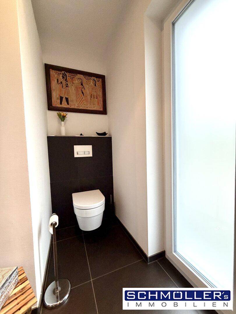 Separate Toilette mit Wand-WC und einem Fenster für natürliche Belüftung.