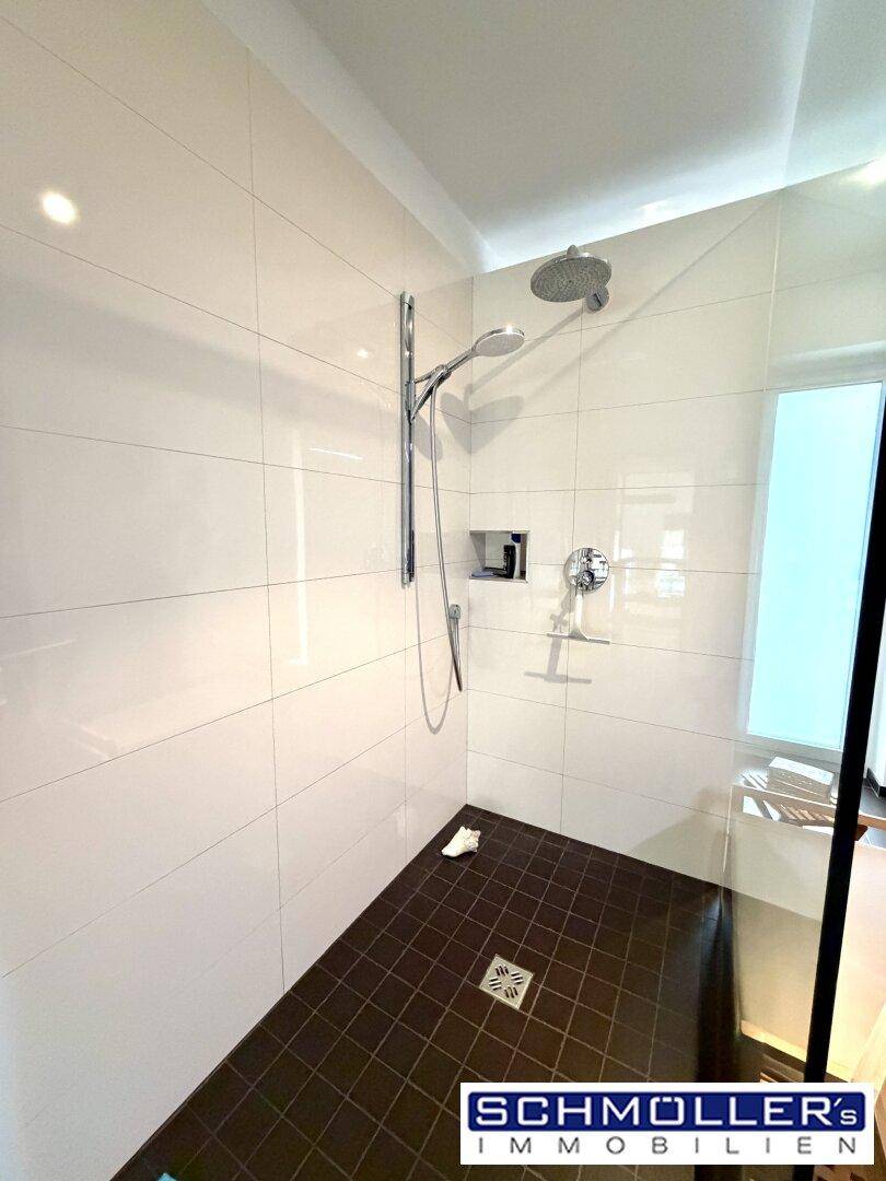 Moderne Duschkabine mit Regendusche und dunklen Bodenfliesen in einem hellen Badezimmer.