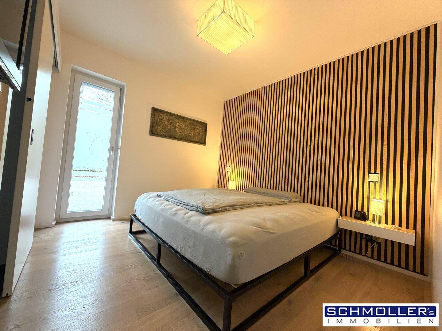 Modernes Schlafzimmer mit Holzwandverkleidung, Doppelbett und Zugang zu einem Außenbereich.