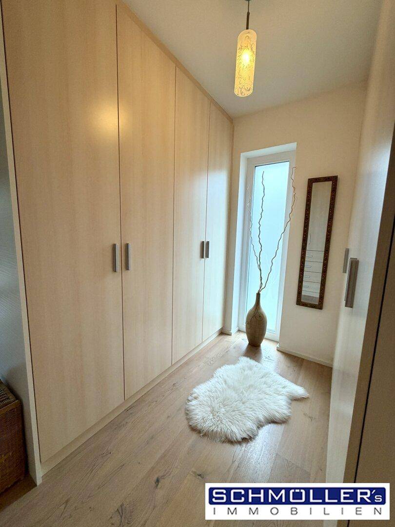 Heller Ankleidebereich mit Einbauschränken, Holzfußboden und einem hohen Fenster.