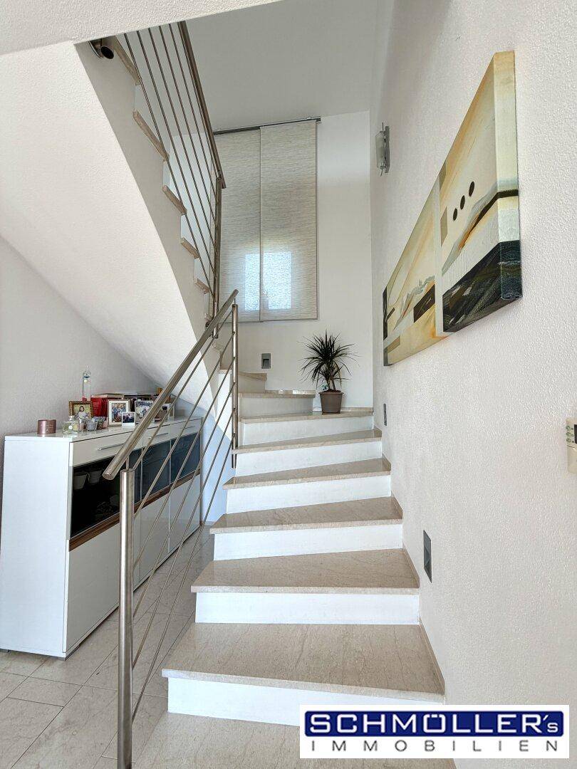 Heller Treppenaufgang mit Fliesenstufen und modernem Edelstahlgeländer, führt in die obere Etage.