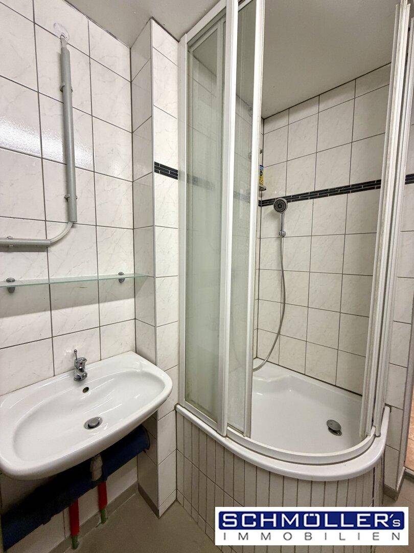 Einfaches Badezimmer mit Duschkabine, Waschbecken und weißen Fliesen.