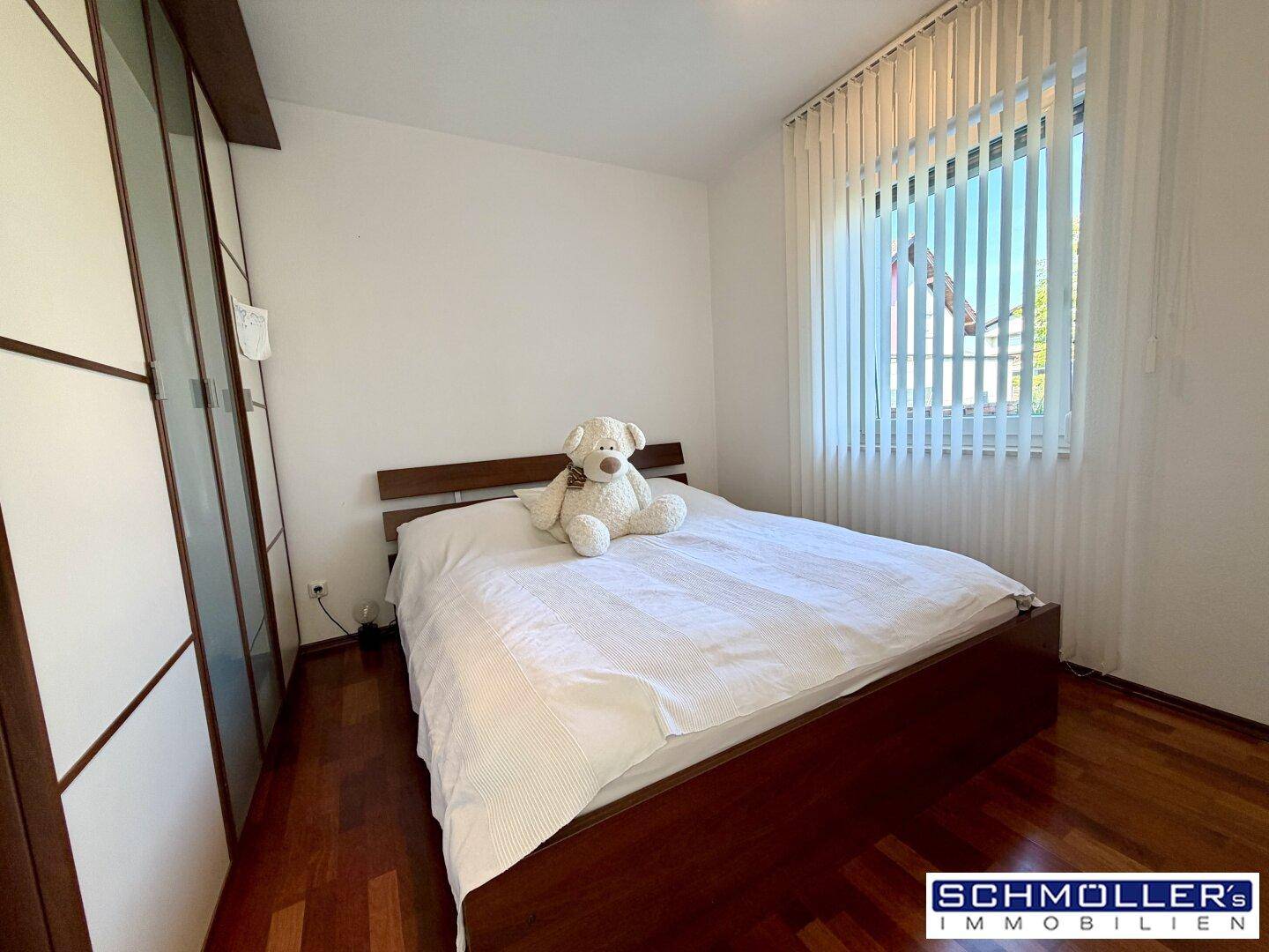 Helles Schlafzimmer mit Holzboden, großem Fenster und integriertem Kleiderschrank.