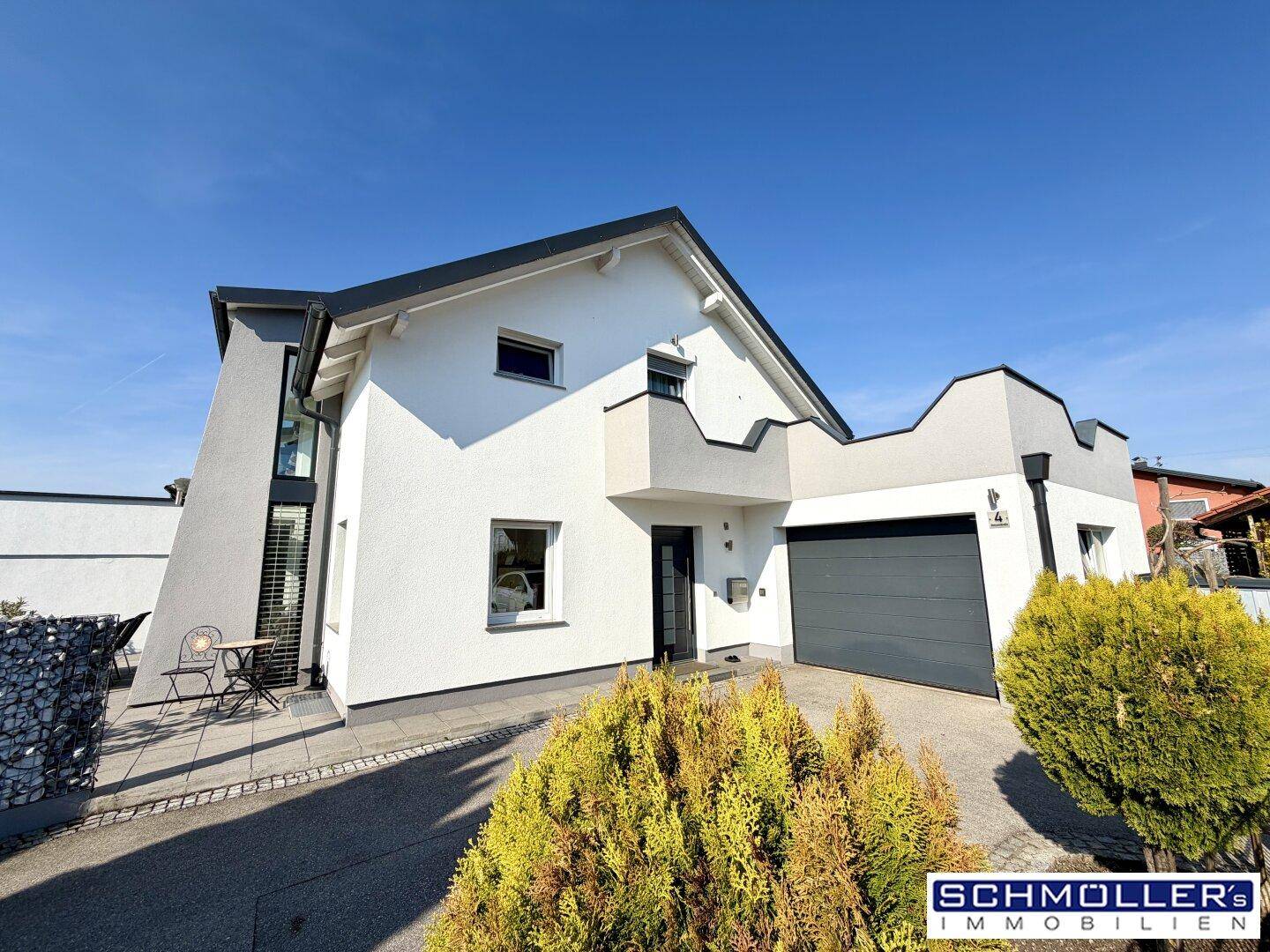 Moderne Hausfassade mit integrierter Garage und gepflegter Auffahrt unter blauem Himmel.