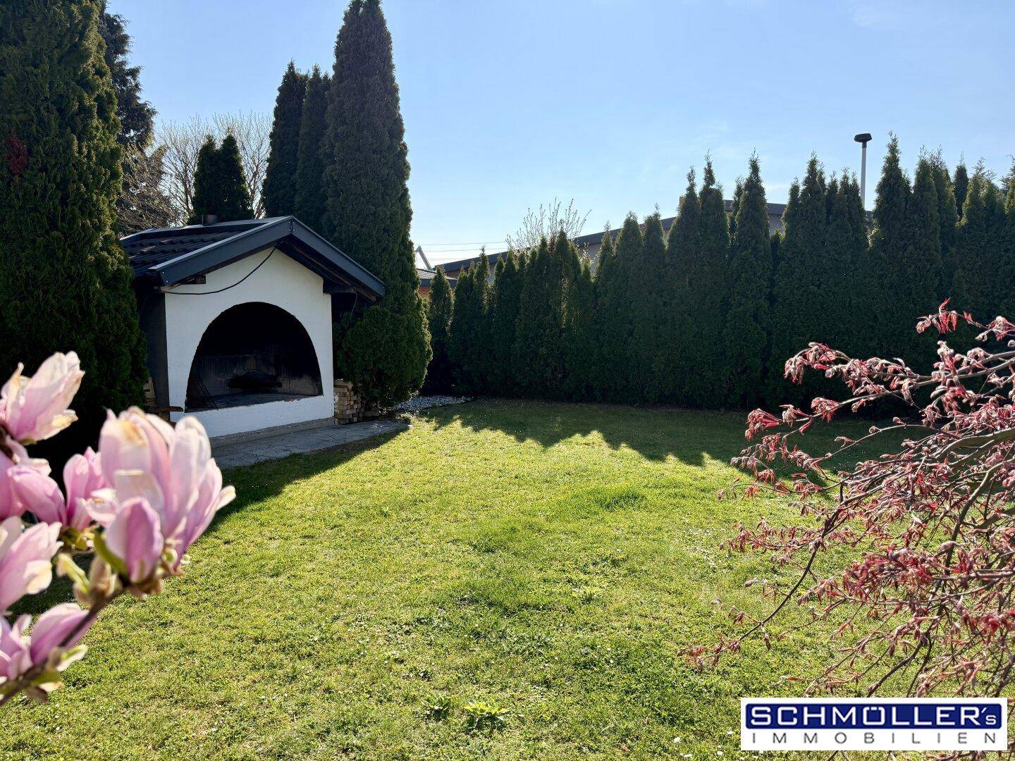Gepflegter Garten mit Rasenfläche, hohen Hecken und einem kleinen Gartenhaus oder Grillbereich.