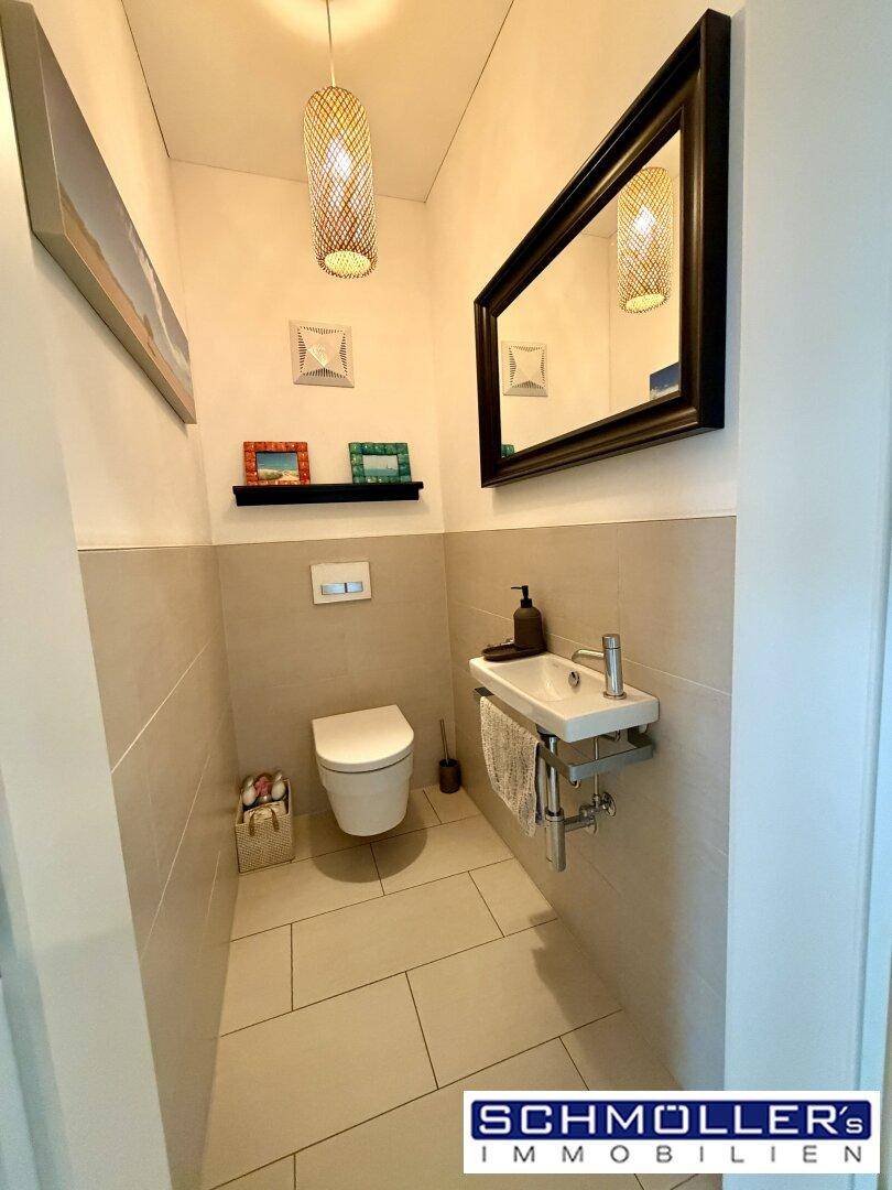 Gäste-WC mit modernem Waschbecken, Spiegel und hellen Wandfliesen.
