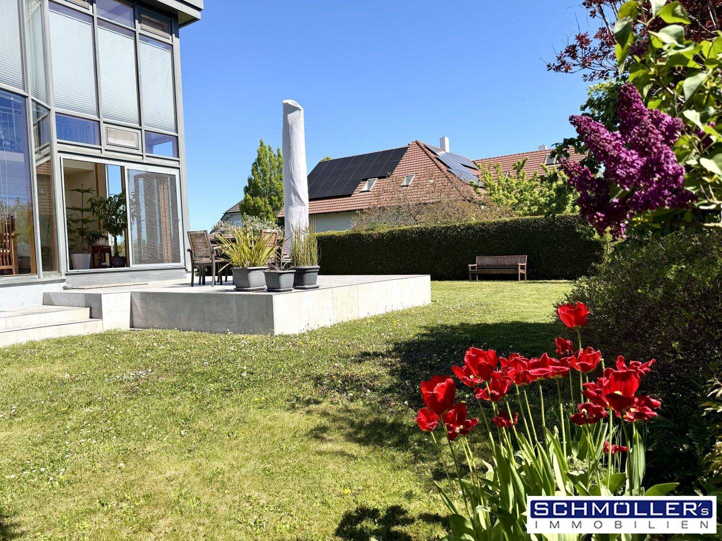 Sonniger Gartenbereich mit gepflegtem Rasen, blühenden Tulpen und einer modernen Terrasse am Haus.
