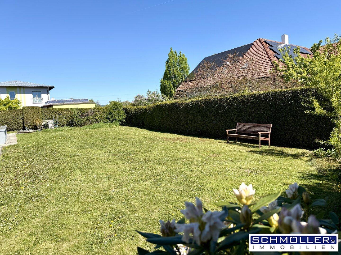 Weitläufiger, gepflegter Garten mit großer Rasenfläche, hoher Hecke und Sitzbank im Grünen.