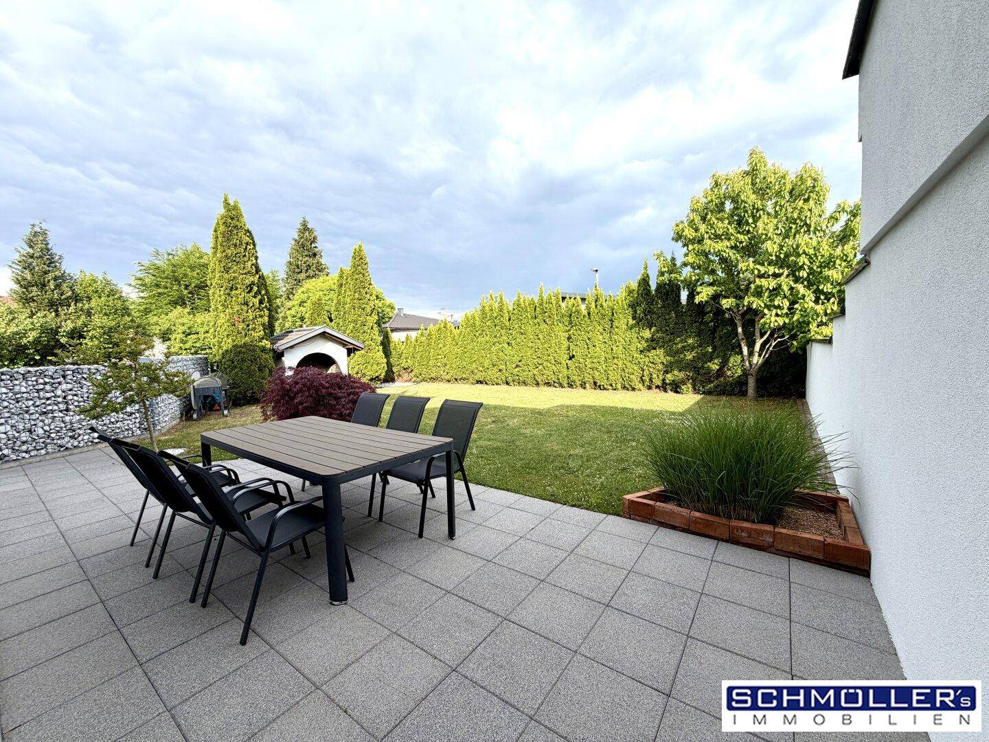 Geräumige Terrasse mit Gartenmöbeln und Blick auf den gepflegten Rasen und die Hecke.