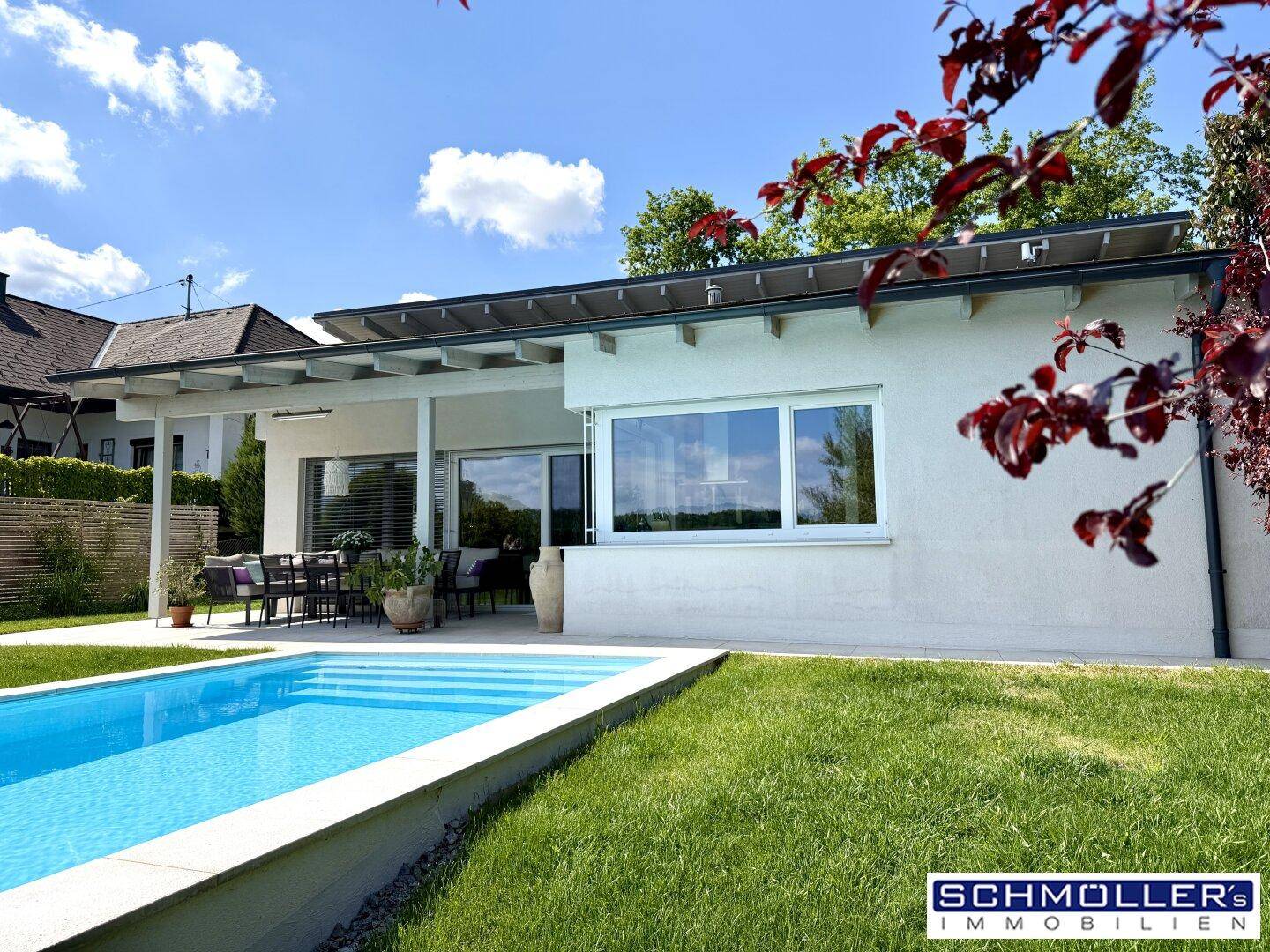 Seitliche Ansicht des modernen Hauses mit Pool und gepflegtem Rasen unter strahlendem Himmel.