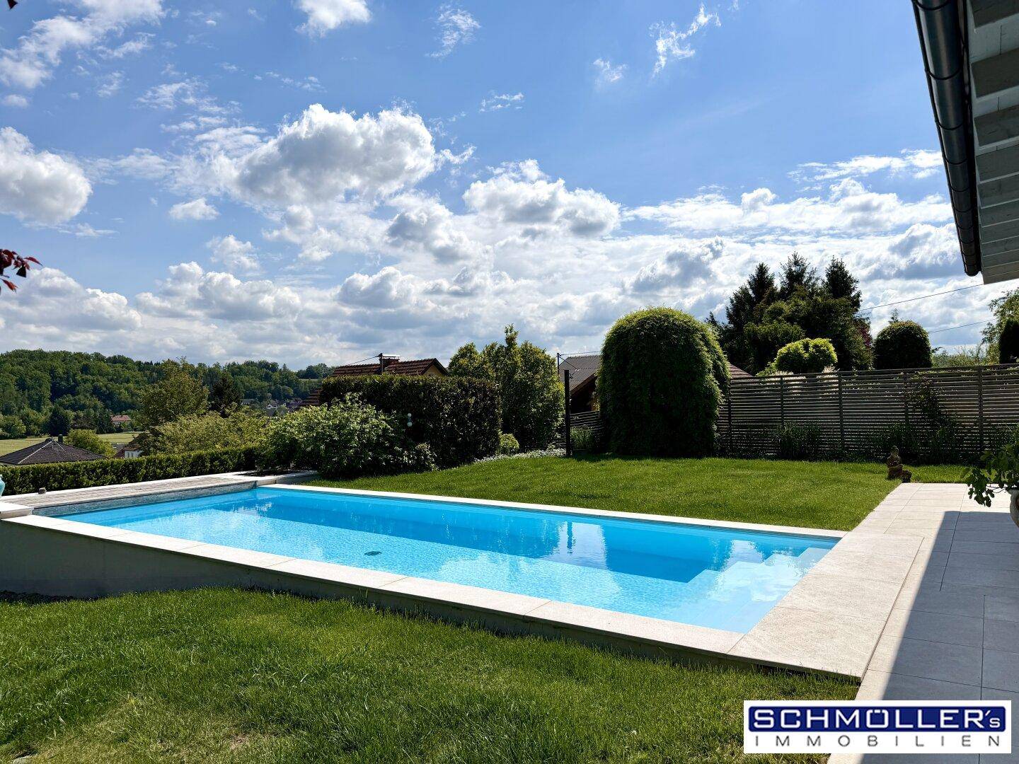 Langer, rechteckiger Swimmingpool im grünen Garten mit weitem Blick in die Landschaft.