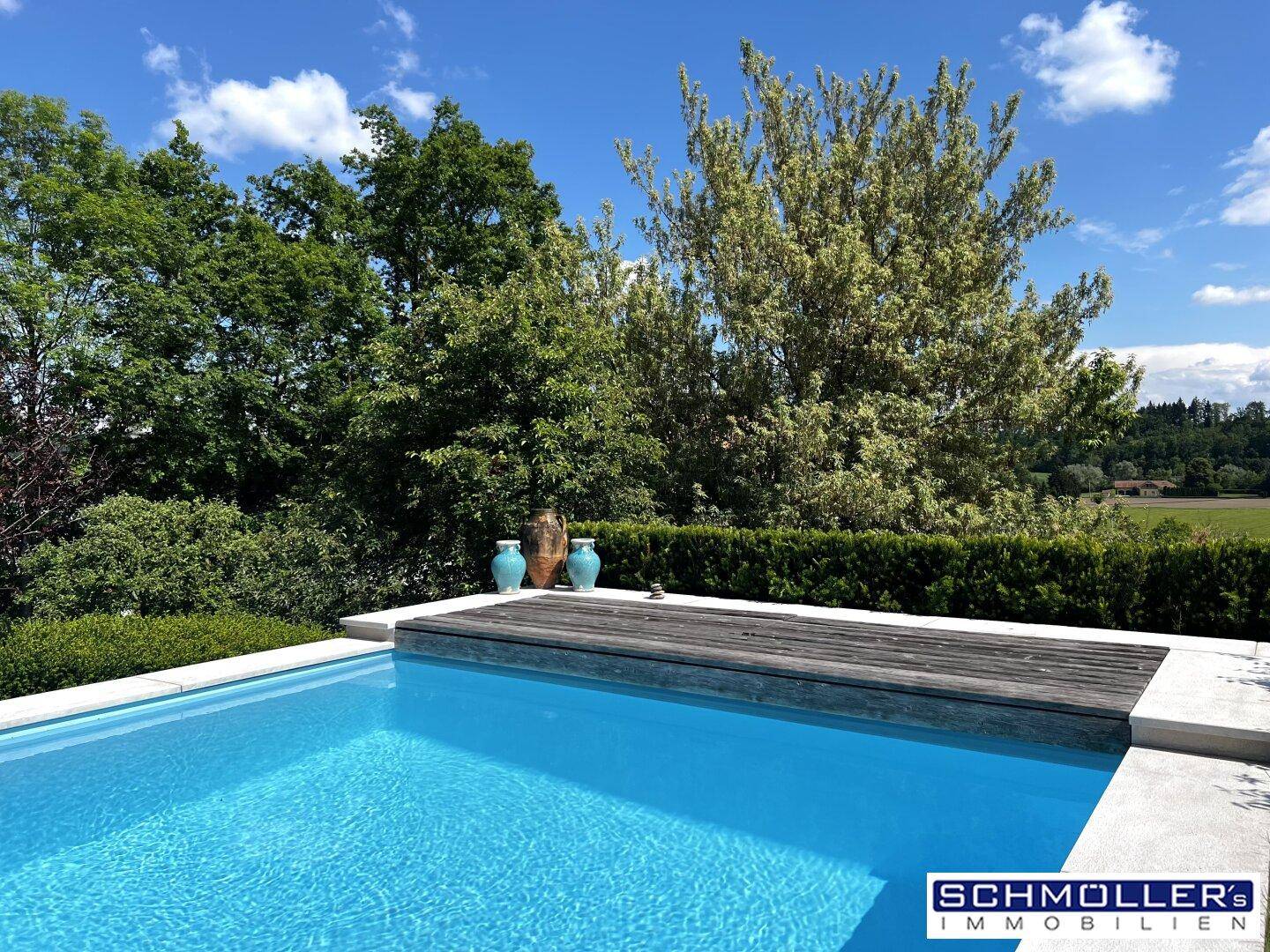 Blauer Swimmingpool mit Holzabdeckung und umgebender Hecke, bietet Privatsphäre und Entspannung.