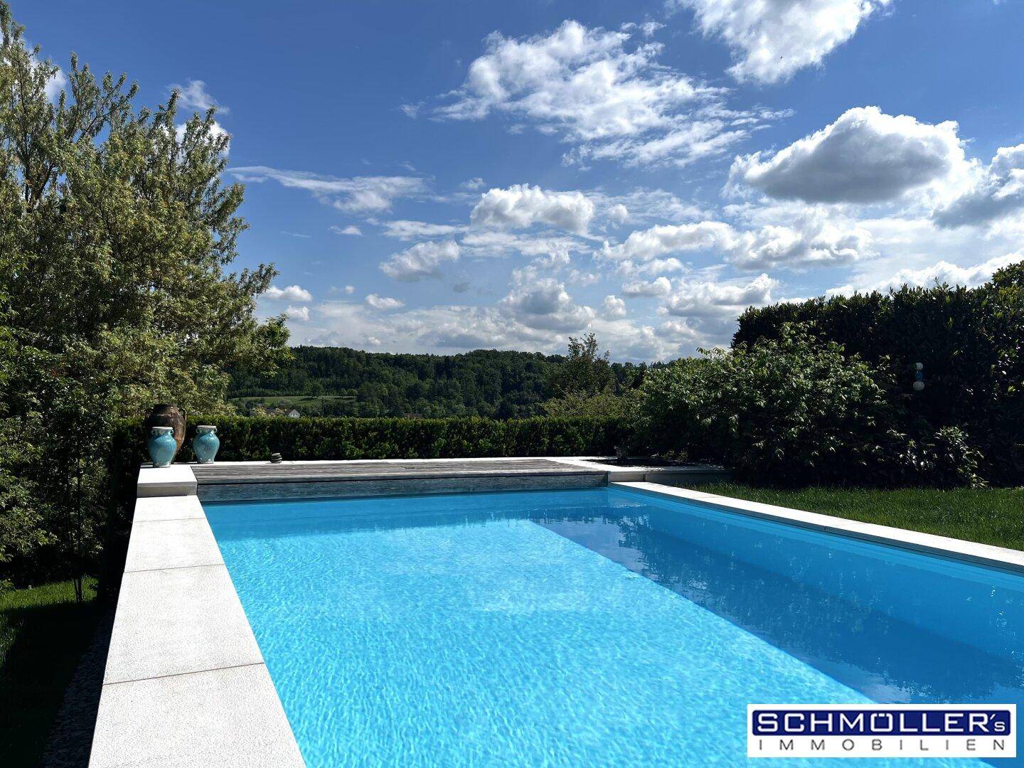 Außenpool mit blauer Wasseroberfläche und weitem Blick auf grüne Hügel und den Himmel.