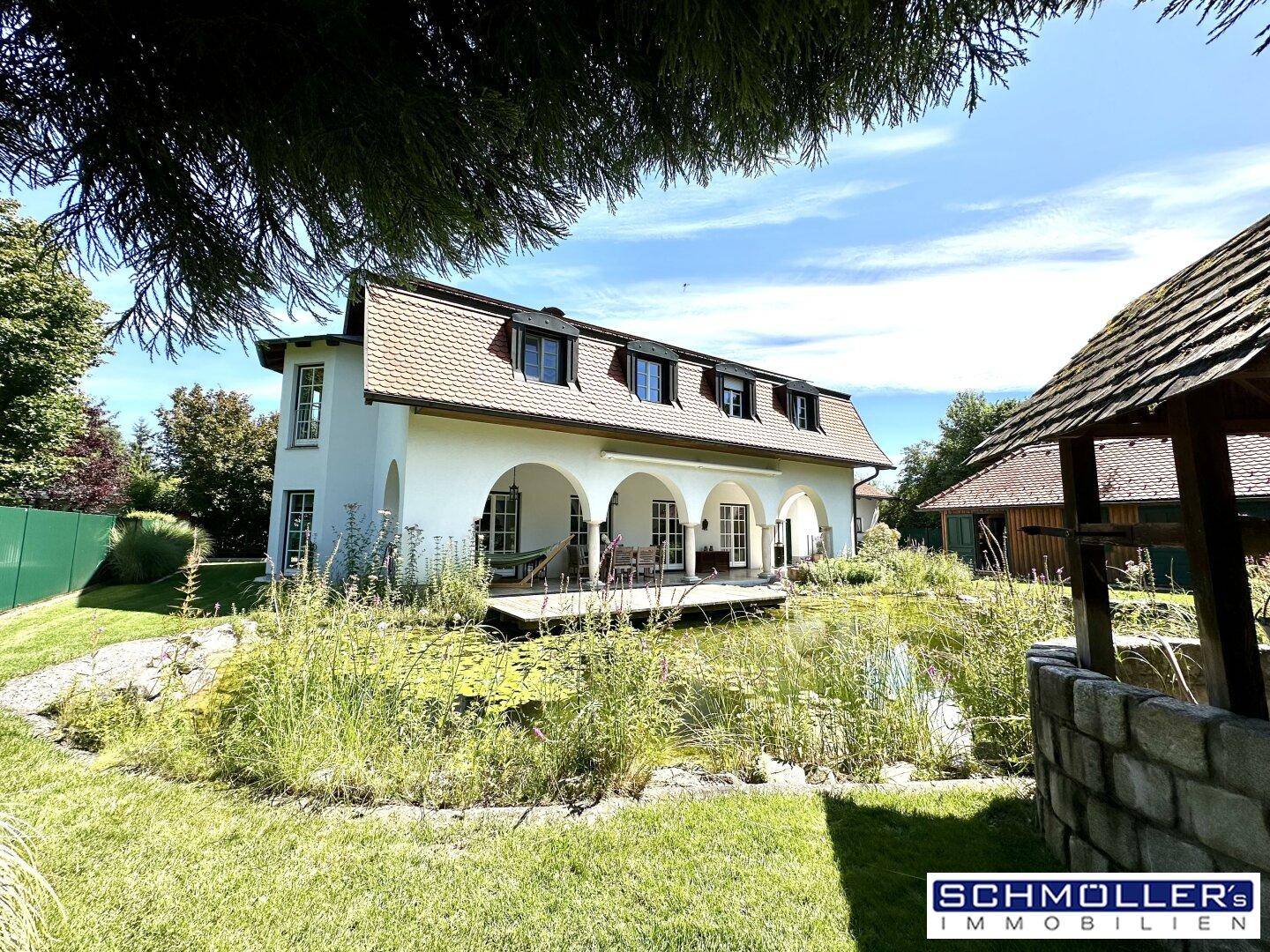 Ansicht des Hauses vom Garten aus mit Teich, Terrasse und üppiger Bepflanzung.