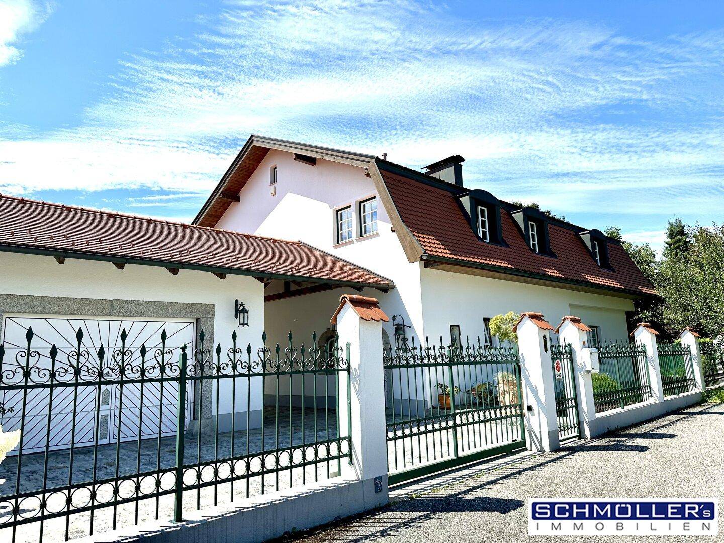 Zufahrt zum Anwesen mit schmiedeeisernem Tor, Garage und gepflegter Fassade.