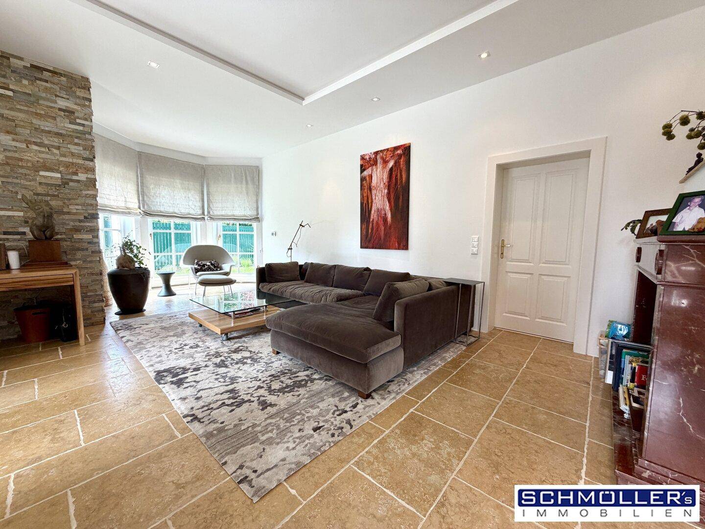 Geräumiges Wohnzimmer mit Steinfassade, großem Sofa und hellen Fliesenböden.
