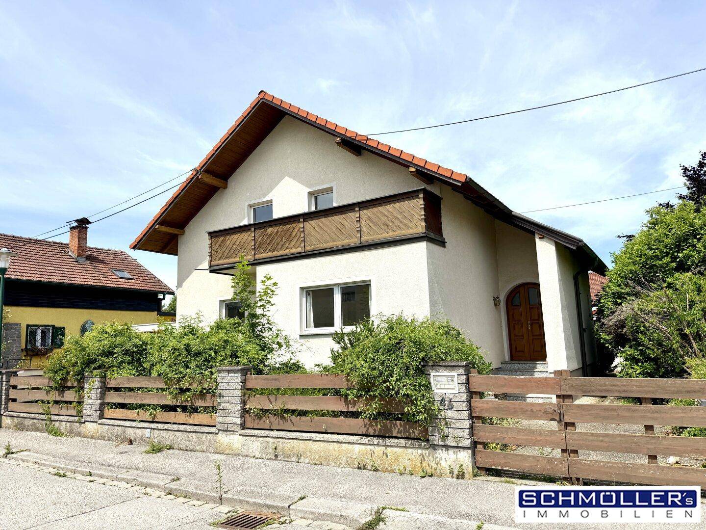 Frontansicht des Hauses mit beiger Fassade, Holzzaun und Balkon im Obergeschoss.
