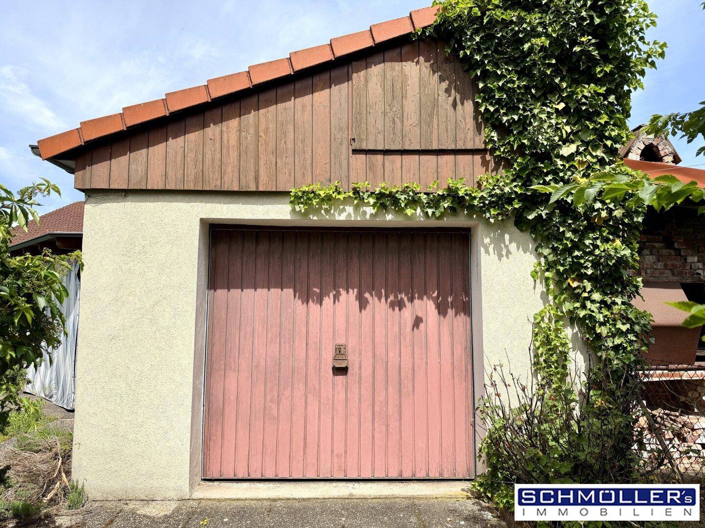 Freistehende Garage mit rustikalem Holztor und Efeubewuchs am Dach und den Wänden.